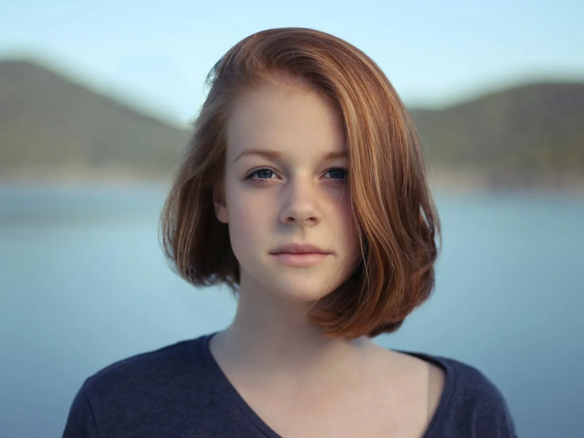 Portrait of a woman with short auburn hair in front of a blurred lake