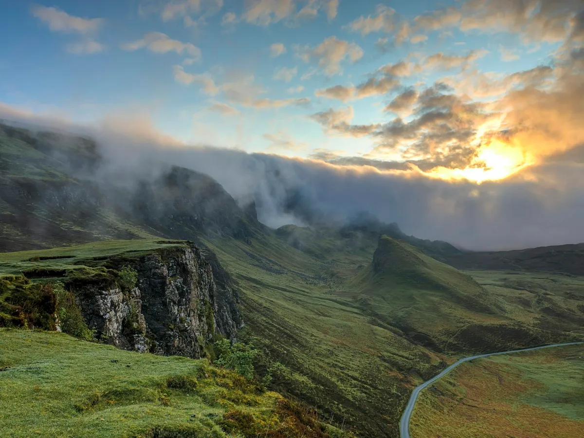Green hills and a winding road under low cloud at sunset