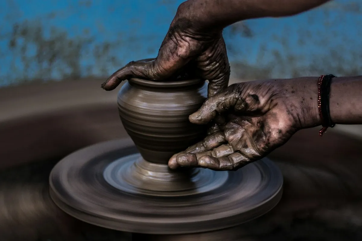 A potter's hands shaping a clay pot on a spinning wheel