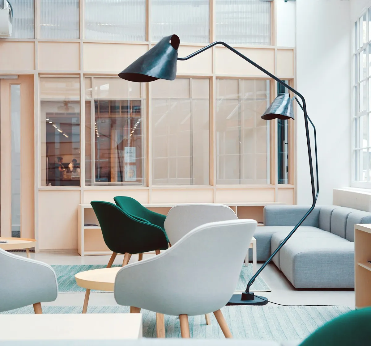 Bright lounge with soft chairs, a floor lamp, and glass meeting rooms behind