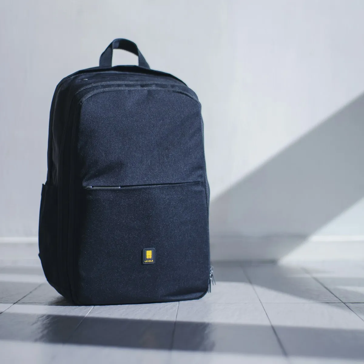 Navy commuter backpack standing on a tiled floor against a white wall