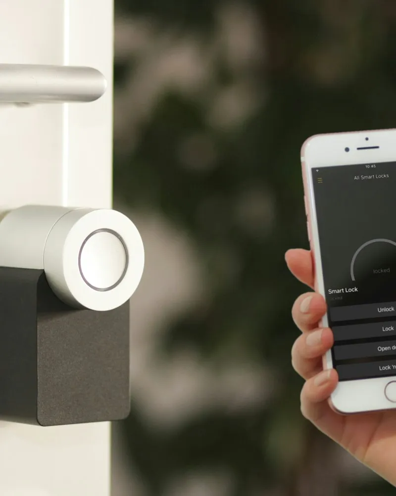 Hand holding a phone next to a smart lock on a door
