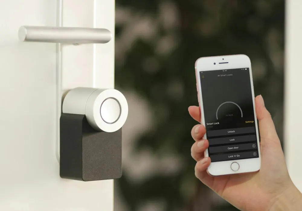 Smart lock fitted to a white door next to a phone showing the lock app