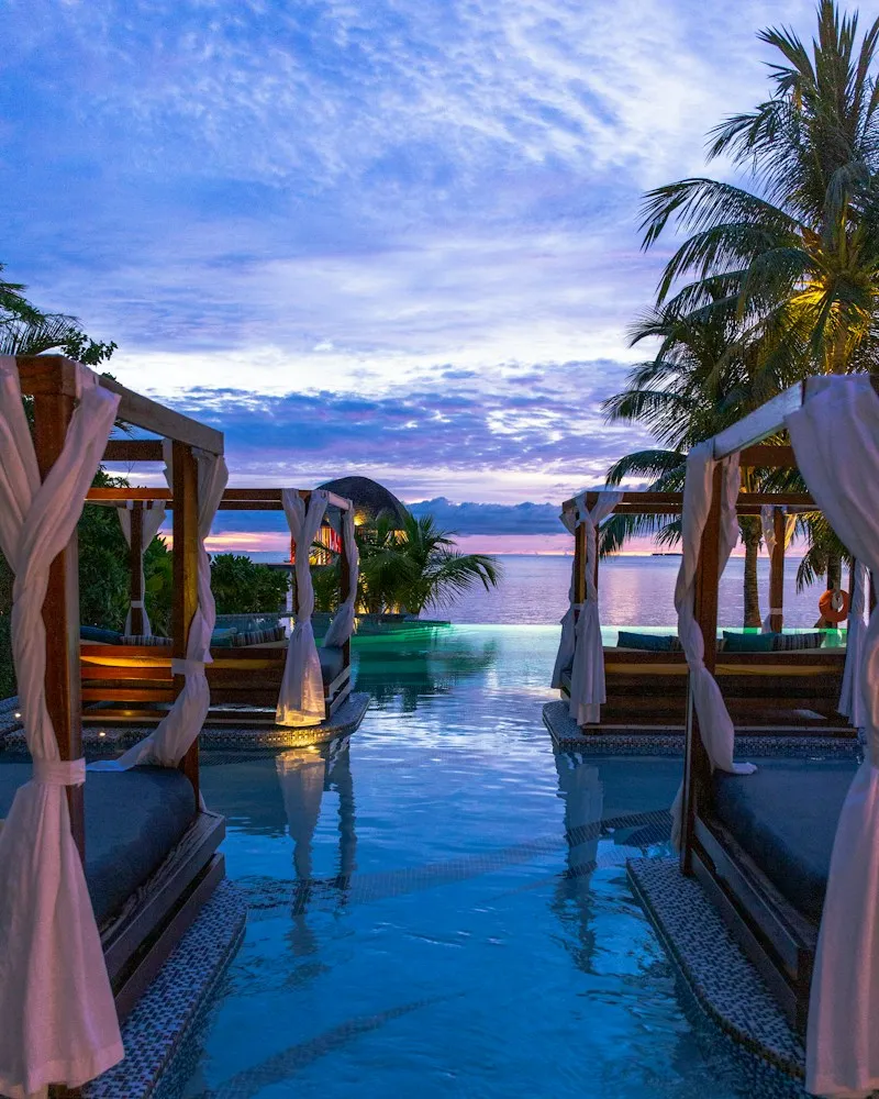Resort pool lined with curtained cabanas at sunset