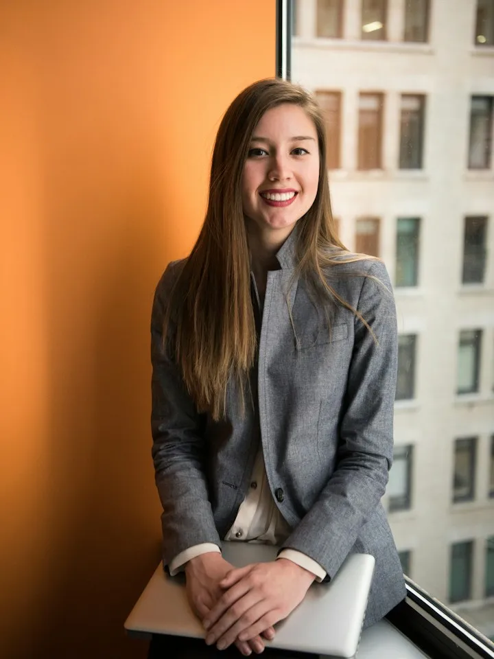 Portrait of a woman in a grey blazer seated by an office window