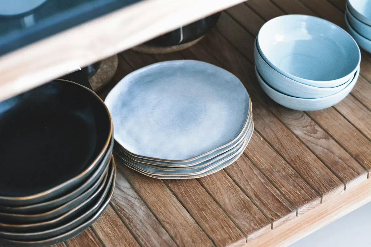 Blue glazed plates and bowls stacked on a wooden shelf