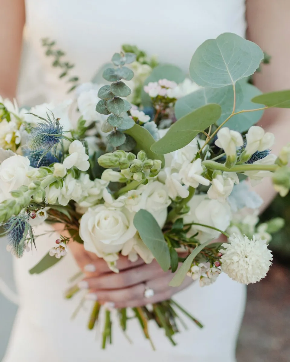 A bride holding a loose bouquet of white flowers and eucalyptus