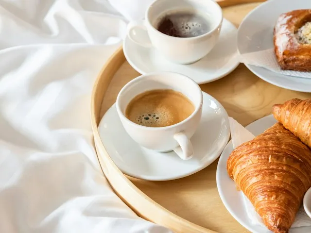 A breakfast tray with coffee and croissants on white bed linen