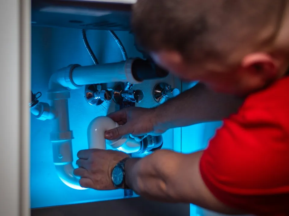 A plumber tightening a fitting on the pipes under a kitchen sink
