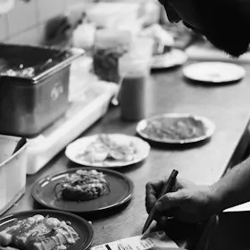 Cook writing notes on the pass beside plated dishes