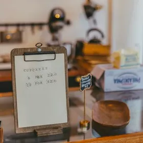 Handwritten price card on a clipboard at a cafe counter